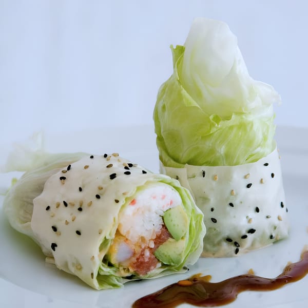 Two fresh Sake Sushi lettuce wraps with tuna, avocado, and shrimp, drizzled with sauce.