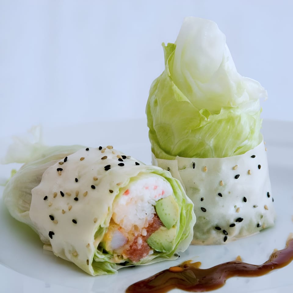 Two fresh Sake Sushi lettuce wraps with tuna, avocado, and shrimp, drizzled with sauce.
