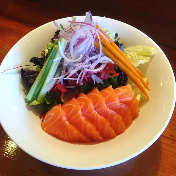 A fresh salmon sashimi salad with red onions, cucumbers, and carrots in a white bowl.