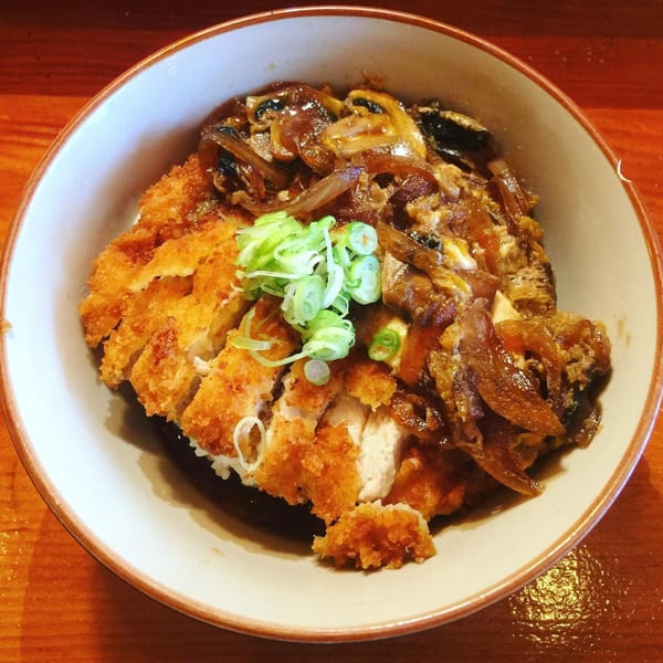 A bowl of katsudon with crispy fried chicken, caramelized onions, and green onions on rice.